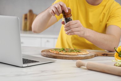 Photo of Man adding pepper on pizza while watching cooking online course in kitchen, closeup. Time for hobby