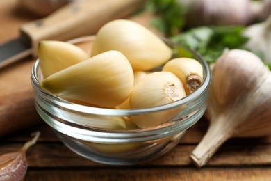 Fresh peeled garlic cloves in bowl on wooden table, closeup. Organic product