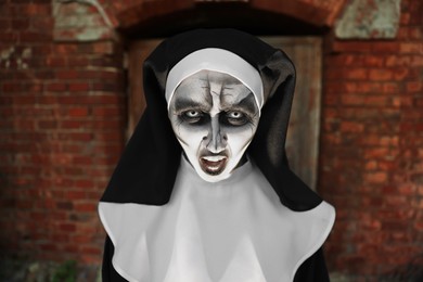 Portrait of scary devilish nun near red brick wall. Halloween party look