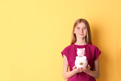 Teen girl with piggy banks on color background. Space for text