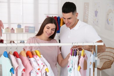 Happy pregnant woman with her husband choosing baby clothes in store. Shopping concept