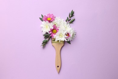 Photo of Brush with colorful flowers of chrysanthemum on violet background, top view. Creative concept