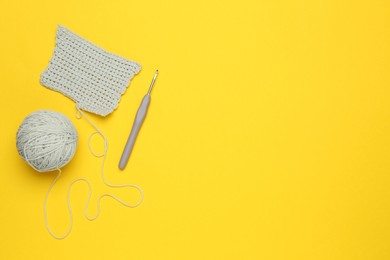 Knitting and crochet hook on yellow background, flat lay. Space for text