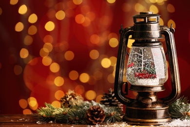Beautiful snow globe in vintage lantern on table against blurred Christmas lights. Space for text