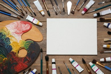 Blank canvas, brushes, paints and palette on wooden table, flat lay. space for text