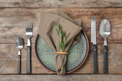 Beautiful table setting with cutlery, napkin and plate on wooden background, top view