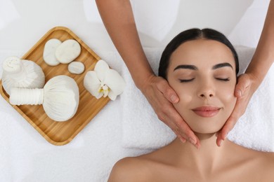 Photo of Young woman receiving facial massage in spa salon, top view