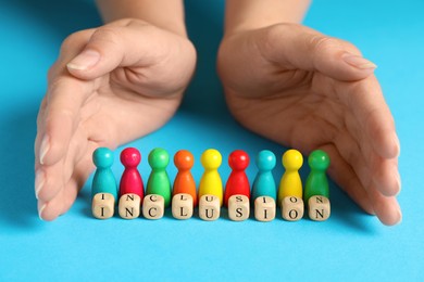 Woman protecting colorful pawns and wooden cubes with word Inclusion on turquoise background, closeup