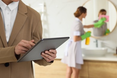 Housekeeping manager with tablet checking maid's work in hotel bathroom, closeup