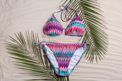Stylish swimsuit and leaves on sand, flat lay. Beach accessory