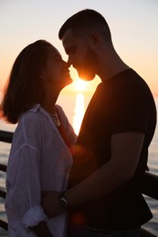 Happy young couple kissing on sea embankment at sunset