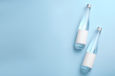 Glass bottles of water with blank labels on light blue background, flat lay. Space for text