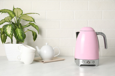 Modern electric kettle, houseplant and tea set on counter in kitchen