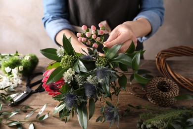 Florist making beautiful bouquet with fresh flowers at wooden table, closeup
