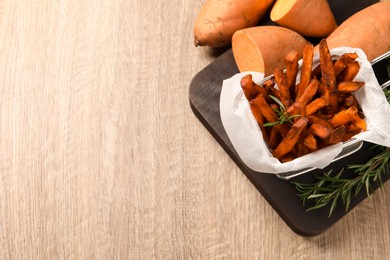 Photo of Frying basket with sweet potato fries on wooden table, above view. Space for text