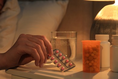 Woman taking pills from nightstand indoors, closeup. Insomnia treatment