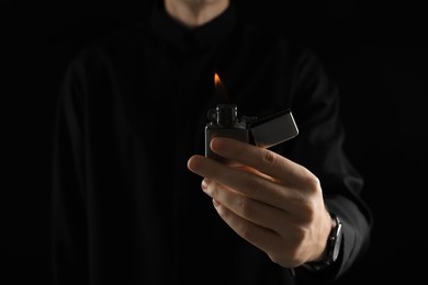 Photo of Man holding lighter with burning flame on black background, closeup. Space for text