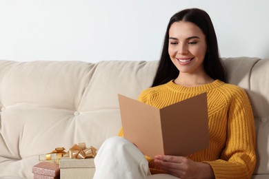 Photo of Happy woman reading greeting card on sofa in living room