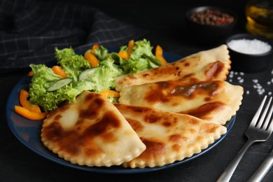 Delicious fried chebureki with vegetables served on black table
