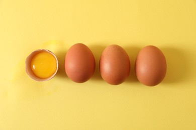 Photo of Cracked and whole chicken eggs on yellow background, flat lay