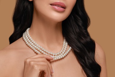 Young woman wearing elegant pearl necklace on brown background, closeup