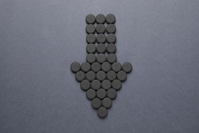 Arrow made of activated charcoal pills on grey background, flat lay. Potent sorbent