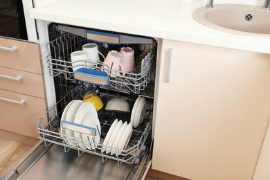 Photo of Open dishwasher with clean tableware in kitchen
