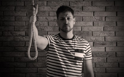 Depressed man with rope noose near brick wall. Suicide concept