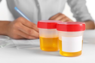 Photo of Closeup view of nurse writing urine analysis results at table, focus on container with sample