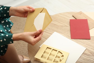 Photo of Woman holding greeting card at wooden table in living room, closeup
