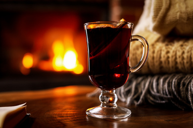 Tasty mulled wine, book, knitwear and blurred fireplace on background