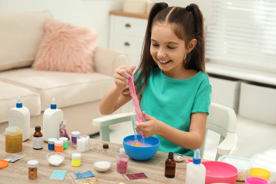 Cute little girl making DIY slime toy at table indoors