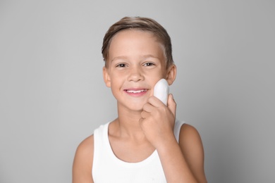 Cute little boy with soap bar on gray background