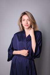Pretty young woman in beautiful dark blue silk robe on grey background