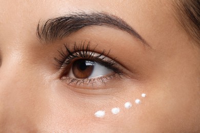 Woman with eye cream on white background, closeup. Skin care