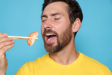 Photo of Handsome man eating sushi with chopsticks on light blue background, closeup
