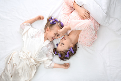 Happy mother and daughter with curlers lying on bed, top view