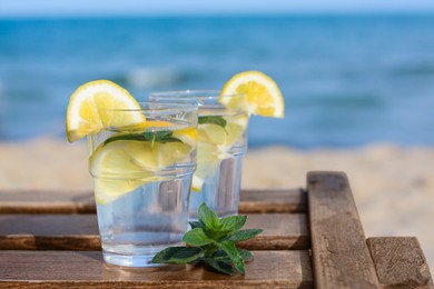 Photo of Refreshing water with lemon and mint on wooden table outdoors, space for text