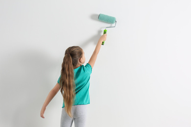 Little child painting with roller brush on white wall indoors. Space for text