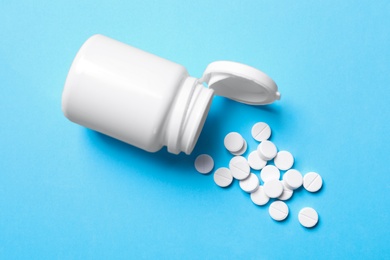 Pills and bottle on light blue background, top view