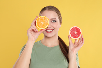 Young woman with cut orange and grapefruit on yellow background. Vitamin rich food
