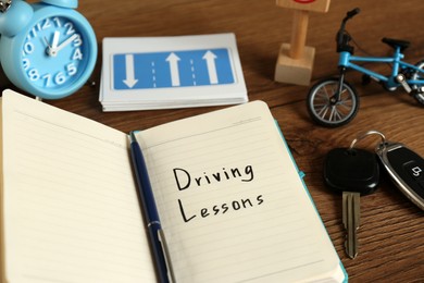 Workbook for driving lessons, pen and car key on wooden table, closeup. Passing license exam