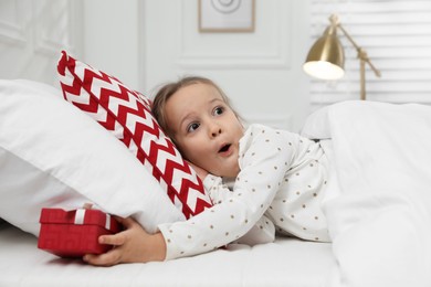 Excited little girl finding gift box under pillow in bed at home. Saint Nicholas day tradition