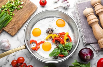Tasty fried eggs with vegetables in pan and ingredients on white marble table, flat lay