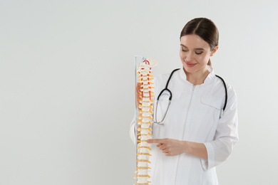 Female orthopedist with human spine model against light background. Space for text