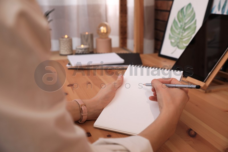 Woman drawing in sketchbook with pencil at wooden table indoors, closeup