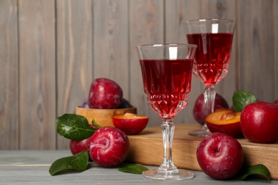 Delicious plum liquor and ripe fruits on grey wooden table, space for text. Homemade strong alcoholic beverage