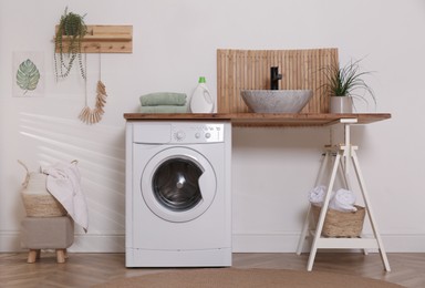Photo of Laundry room interior with modern washing machine and stylish vessel sink on wooden countertop