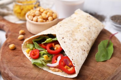 Photo of Delicious hummus wrap with vegetables on wooden board, closeup