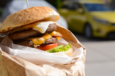 Photo of Delicious burger in paper wrap on city street, closeup. Space for text